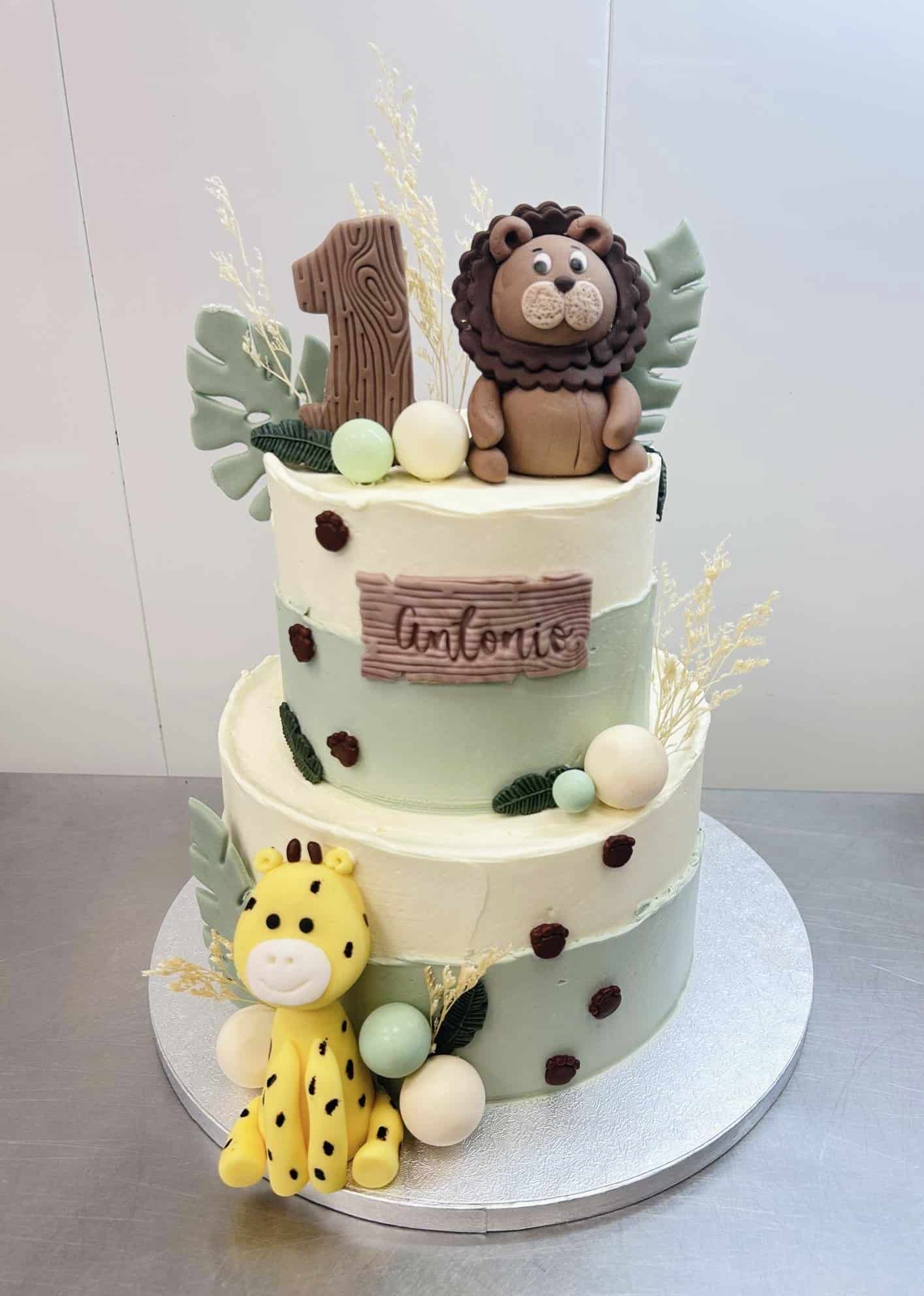 Gâteau d'anniversaire à deux étages thème safari 1 an, décoré d'un lion, d'une girafe et du prénom "Antonio".